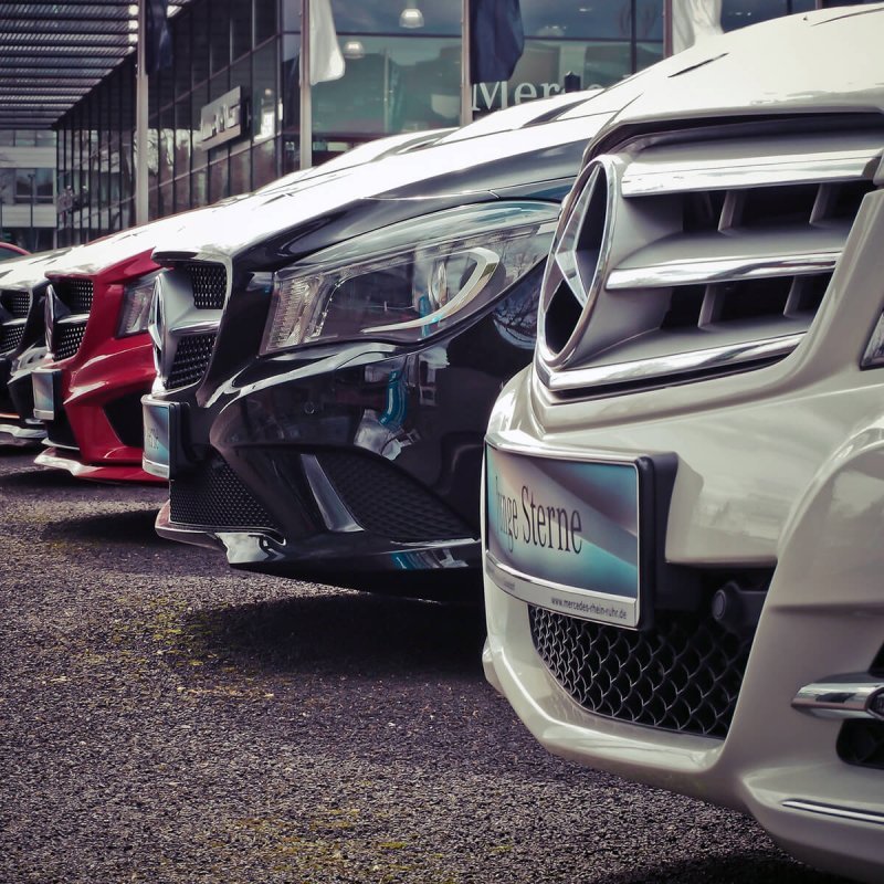 A row of cars parked on the street, showcasing various models and colors. The vehicles are neatly aligned, each displaying their own unique design features such as wheels, headlights, and bumpers.