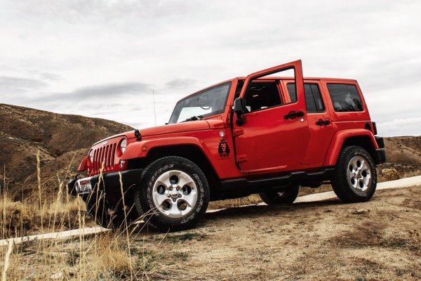 A red jeep parked on a dirt road surrounded by grass and under a clear sky.