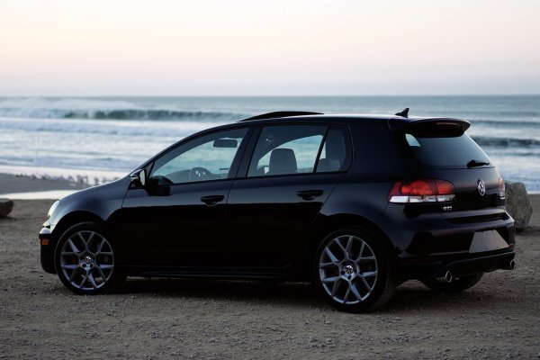 A car parked on a beach with the ocean in the background and blue sky above.